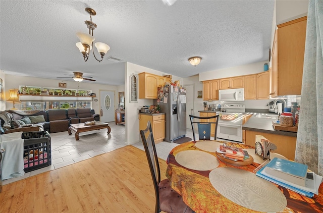 dining space with a textured ceiling, ceiling fan with notable chandelier, sink, and light hardwood / wood-style flooring