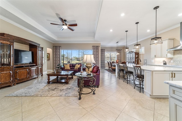 tiled living room with a tray ceiling, ceiling fan, and ornamental molding