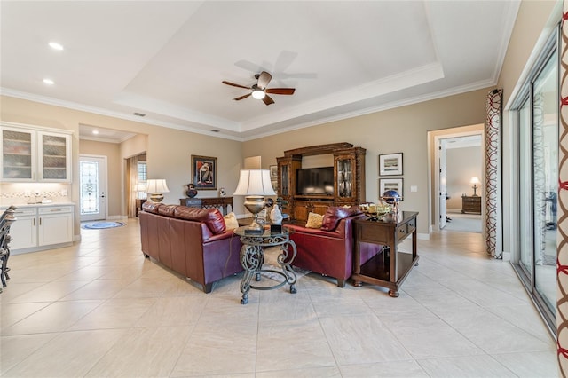 tiled living room with a raised ceiling, ceiling fan, and ornamental molding