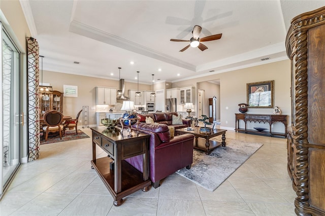 living room featuring a tray ceiling, ceiling fan, light tile patterned floors, and ornamental molding