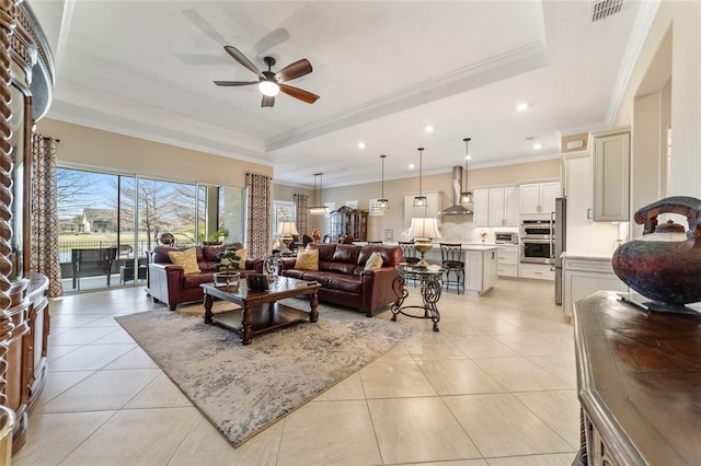 living room featuring a tray ceiling, ceiling fan, light tile patterned floors, and ornamental molding