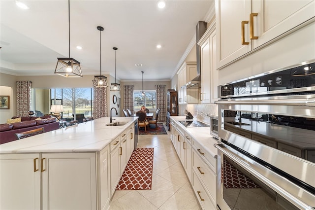 kitchen featuring a kitchen island with sink, sink, double oven, tasteful backsplash, and decorative light fixtures