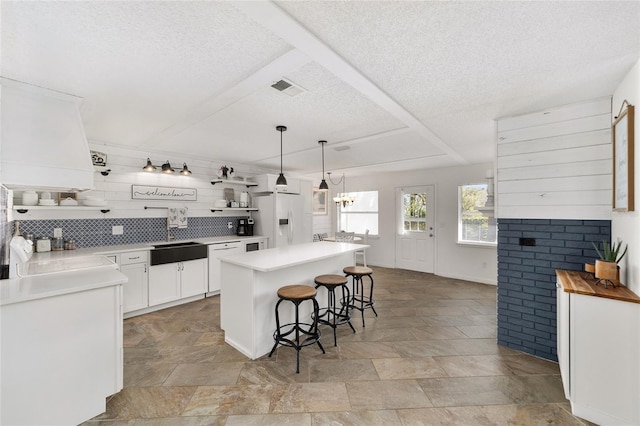 kitchen featuring white appliances, decorative light fixtures, white cabinets, a center island, and a breakfast bar area