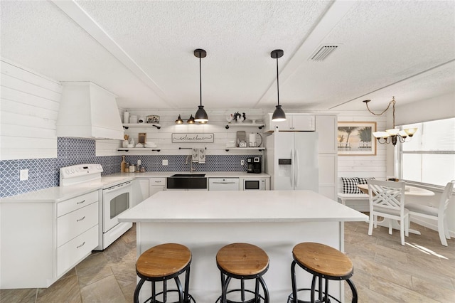 kitchen with premium range hood, white cabinetry, hanging light fixtures, and white appliances