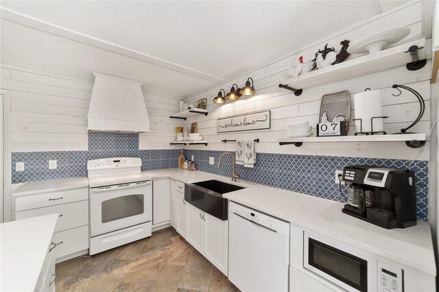 kitchen featuring custom exhaust hood, white appliances, sink, a textured ceiling, and white cabinetry