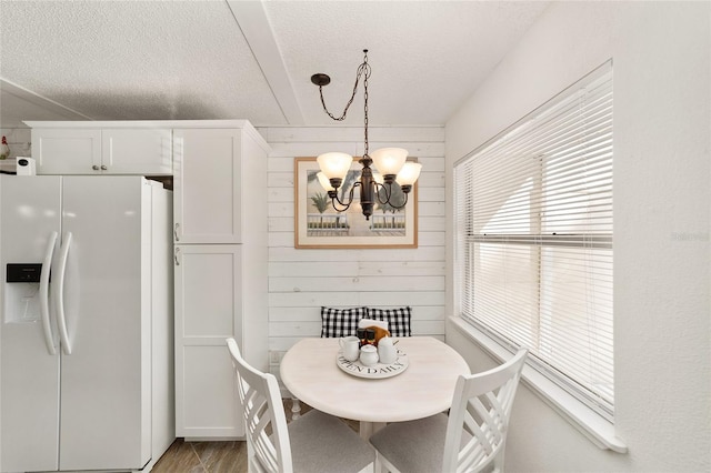 dining space featuring wood walls, light wood-type flooring, a textured ceiling, and a notable chandelier