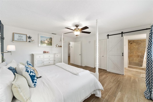 bedroom with ceiling fan, a barn door, light hardwood / wood-style floors, and a textured ceiling