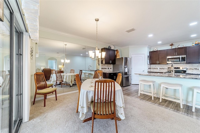 dining room with a notable chandelier, light colored carpet, ornamental molding, and sink