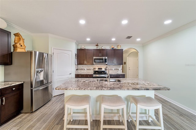 kitchen with appliances with stainless steel finishes, dark brown cabinetry, a center island with sink, and sink