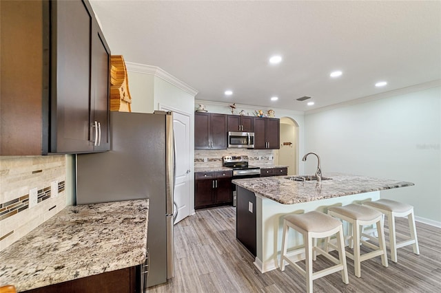 kitchen with light stone countertops, tasteful backsplash, stainless steel appliances, sink, and an island with sink