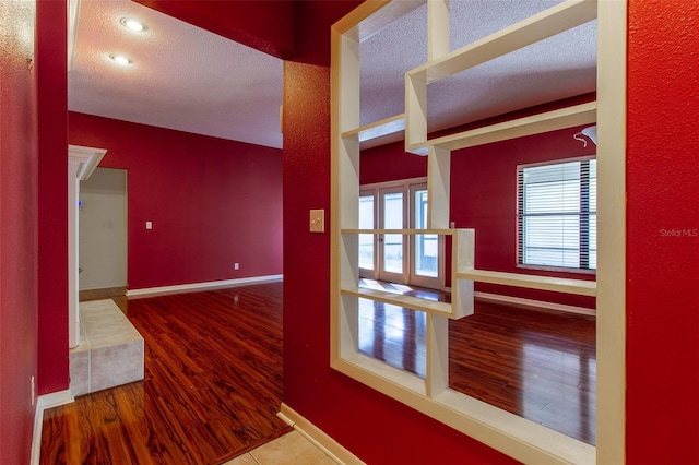 hall with wood-type flooring, a textured ceiling, and french doors