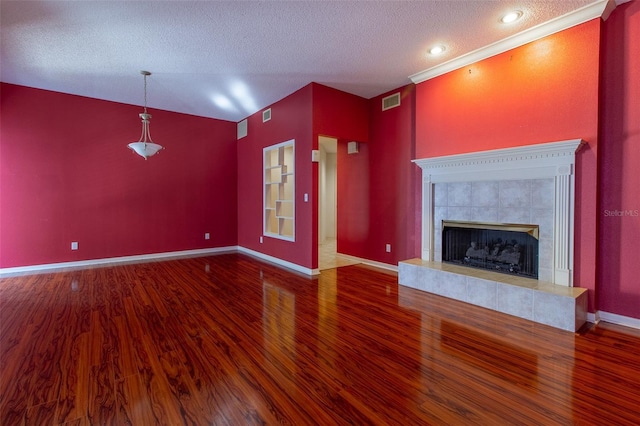 unfurnished living room with wood-type flooring, a textured ceiling, crown molding, and a tiled fireplace