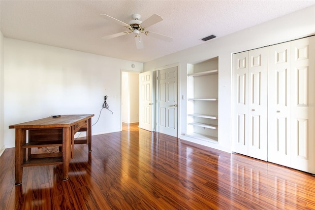 unfurnished dining area with a textured ceiling, dark hardwood / wood-style flooring, built in features, and ceiling fan