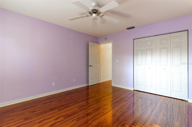 unfurnished bedroom with ceiling fan, a closet, dark wood-type flooring, and a textured ceiling