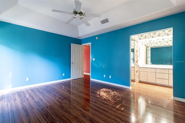 unfurnished bedroom featuring ensuite bath, a tray ceiling, vaulted ceiling, ceiling fan, and hardwood / wood-style floors