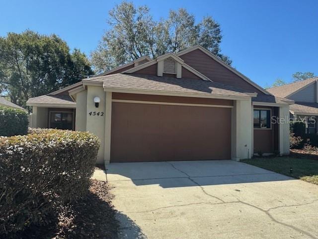 ranch-style home with an attached garage, roof with shingles, concrete driveway, and stucco siding