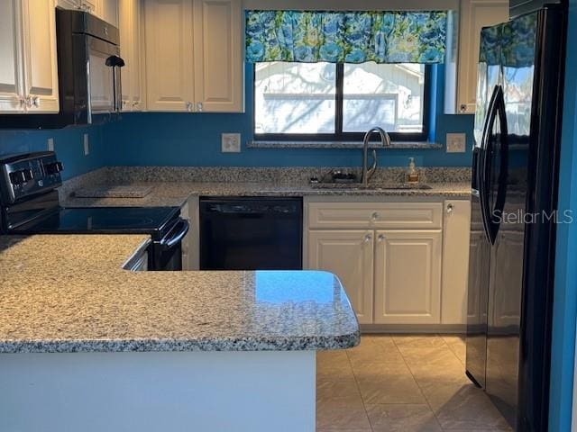 kitchen featuring a peninsula, a sink, white cabinets, light stone countertops, and black appliances