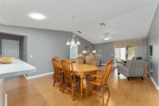 dining area with a textured ceiling, ceiling fan with notable chandelier, light hardwood / wood-style flooring, and vaulted ceiling