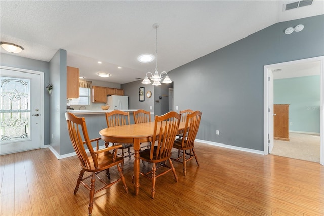 dining space featuring light hardwood / wood-style flooring, vaulted ceiling, and an inviting chandelier