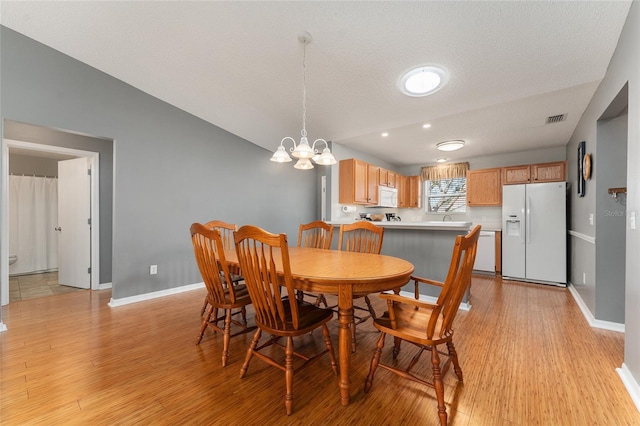 dining area with a textured ceiling, a chandelier, vaulted ceiling, and light wood-type flooring