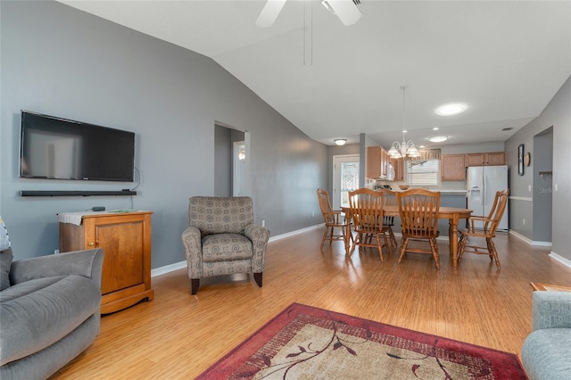 dining space featuring light hardwood / wood-style flooring, ceiling fan with notable chandelier, and vaulted ceiling