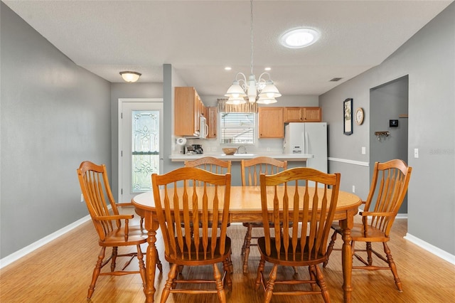 dining room with an inviting chandelier, sink, a textured ceiling, and light hardwood / wood-style flooring