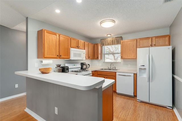 kitchen featuring kitchen peninsula, a textured ceiling, white appliances, sink, and light hardwood / wood-style flooring