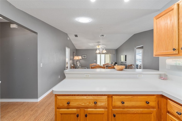 kitchen with kitchen peninsula, light wood-type flooring, a textured ceiling, vaulted ceiling, and ceiling fan