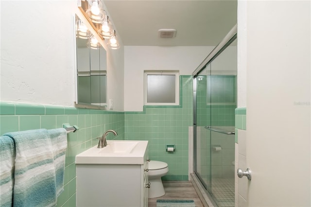 bathroom featuring vanity, a shower with door, and tile walls