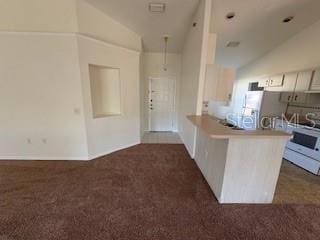 kitchen with kitchen peninsula, white appliances, lofted ceiling, and dark colored carpet