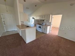 kitchen featuring stove, white refrigerator, kitchen peninsula, vaulted ceiling, and white cabinetry