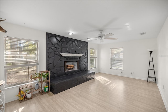 living room with a wealth of natural light, a fireplace, ceiling fan, and light wood-type flooring