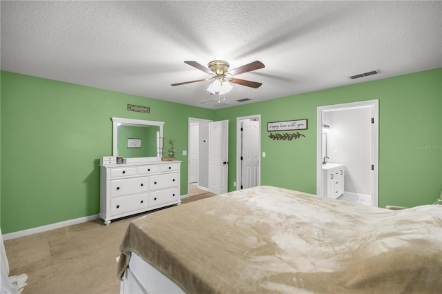 bedroom with ceiling fan, light colored carpet, a textured ceiling, and connected bathroom