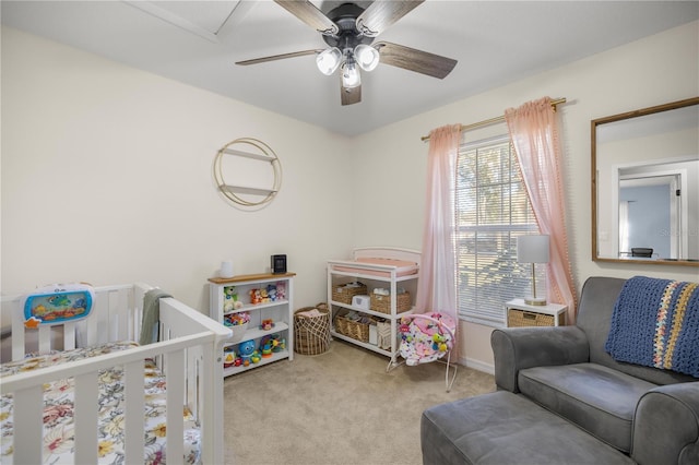 bedroom featuring a nursery area, light colored carpet, and ceiling fan