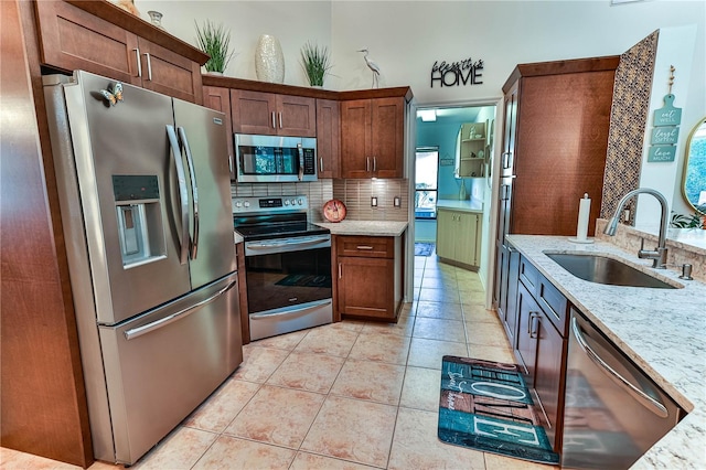 kitchen featuring tasteful backsplash, sink, light tile patterned floors, light stone counters, and stainless steel appliances