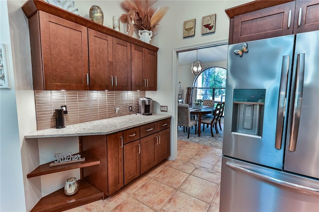 kitchen featuring light tile patterned floors, stainless steel fridge, tasteful backsplash, light stone countertops, and decorative light fixtures