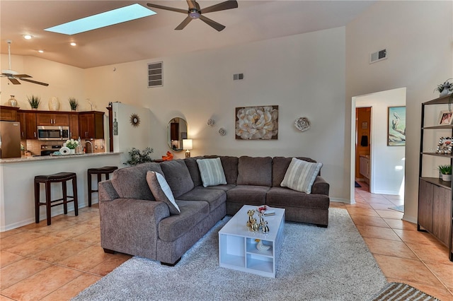 living room featuring light tile patterned flooring, high vaulted ceiling, ceiling fan, and a skylight