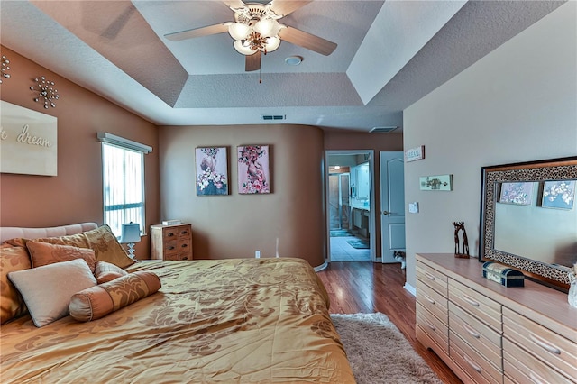 bedroom with ensuite bathroom, dark hardwood / wood-style floors, ceiling fan, a tray ceiling, and a textured ceiling