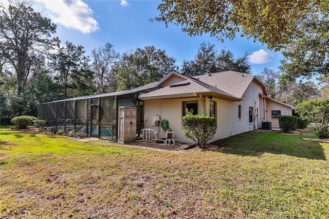 rear view of property with a yard, central air condition unit, and a lanai