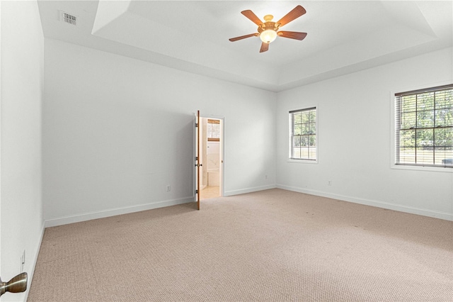 carpeted spare room with a raised ceiling and ceiling fan