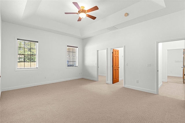 unfurnished bedroom with light colored carpet, a raised ceiling, and ceiling fan