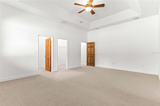 unfurnished bedroom with a spacious closet, ceiling fan, carpet floors, a tray ceiling, and a closet