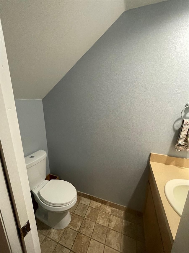 bathroom with vanity, toilet, and lofted ceiling