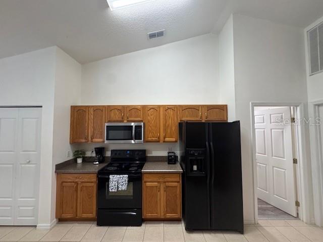 kitchen with light tile patterned flooring, high vaulted ceiling, and black appliances