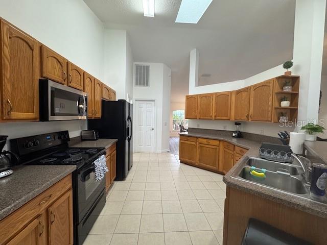 kitchen with a skylight, a high ceiling, light tile patterned flooring, black appliances, and sink