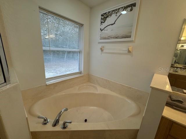 bathroom featuring a relaxing tiled tub, a wealth of natural light, and vanity