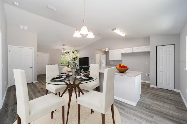 dining space with sink, ceiling fan with notable chandelier, wood-type flooring, and lofted ceiling