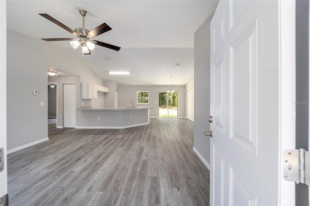 unfurnished living room featuring ceiling fan with notable chandelier, light hardwood / wood-style flooring, vaulted ceiling, and sink