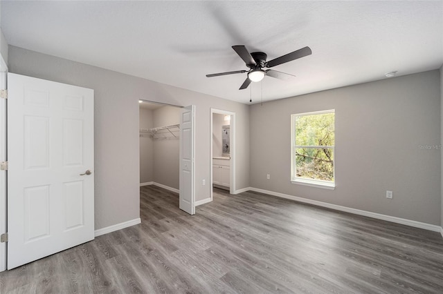 unfurnished bedroom featuring a walk in closet, ceiling fan, a closet, and hardwood / wood-style flooring