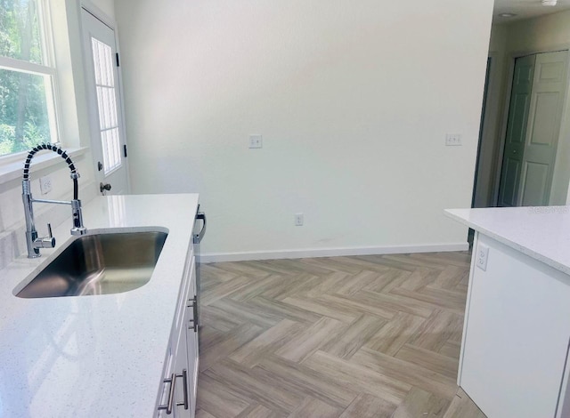 kitchen with white cabinetry, light countertops, baseboards, and a sink
